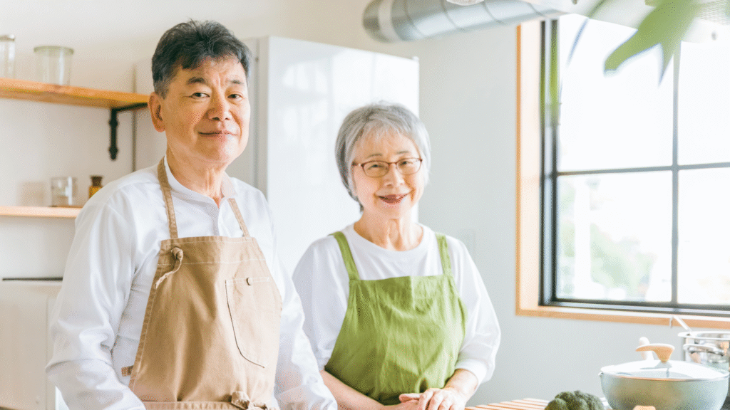 エプロンをつけて笑顔でキッチンに立っている老夫婦