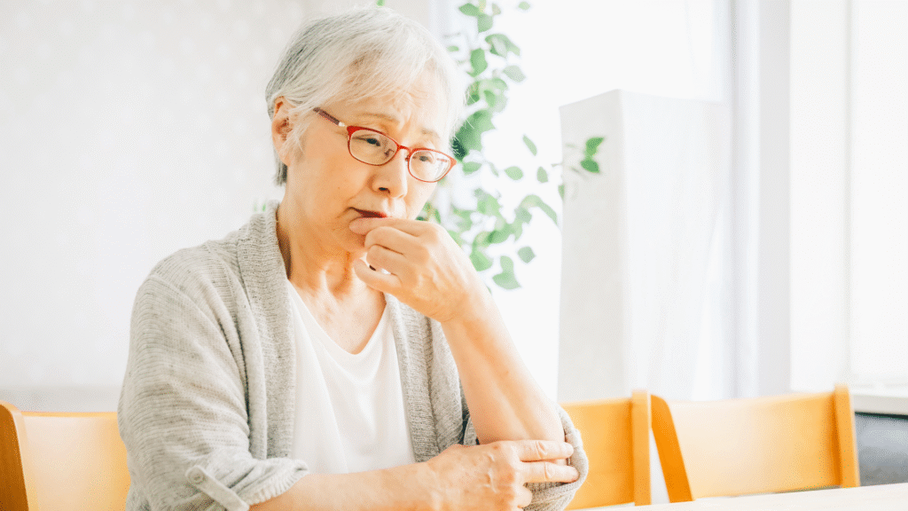 ダイニングテーブルにすわって悩んでいる眼鏡をかけた高齢女性