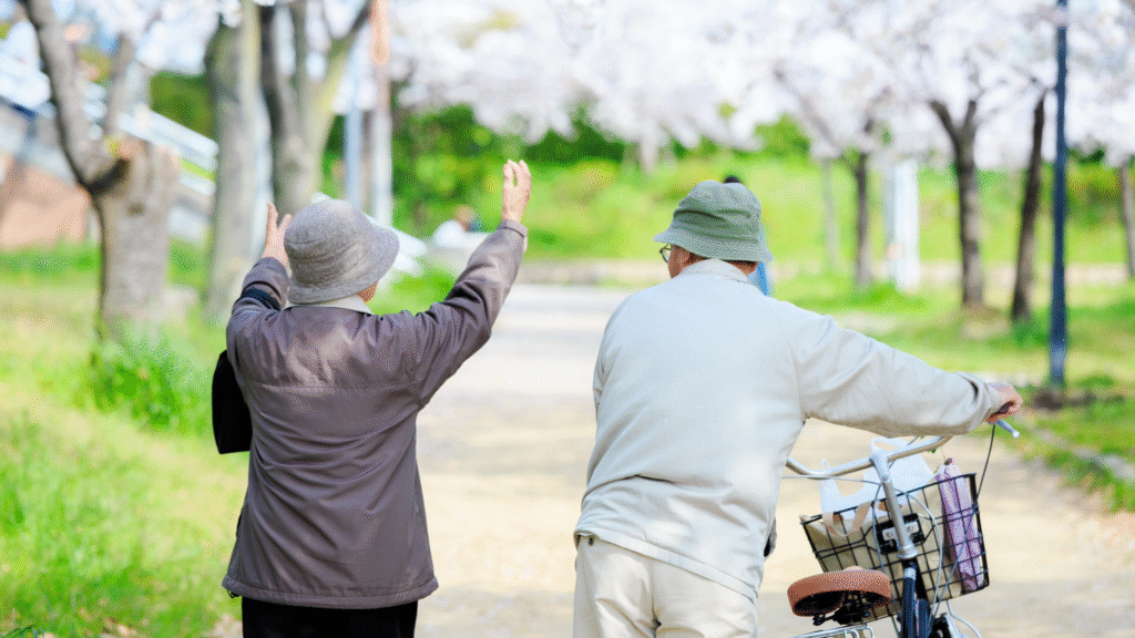 自転車をおして天気の良い日に道を歩いている老夫婦の後ろ姿